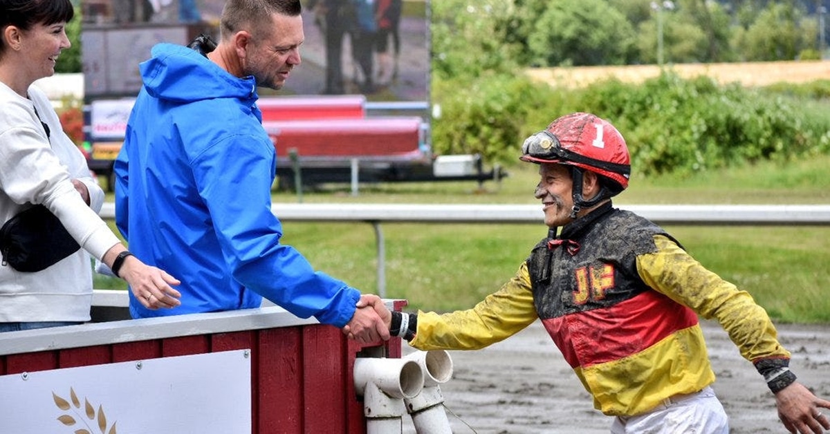 A racehorse owner shaking a jockey's hand at the track.