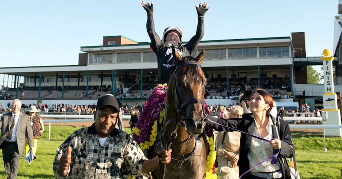 A jockey raising his hands in the air on the way to the winner's circle.