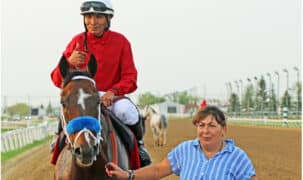 A woman leading a racehorse and jockey into the winner's circle.