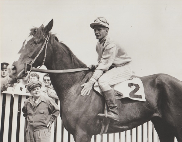 Old black-and-white photo of a jockey patting a raehorse.