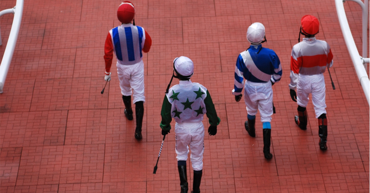 A group of jockeys walking toward the track.