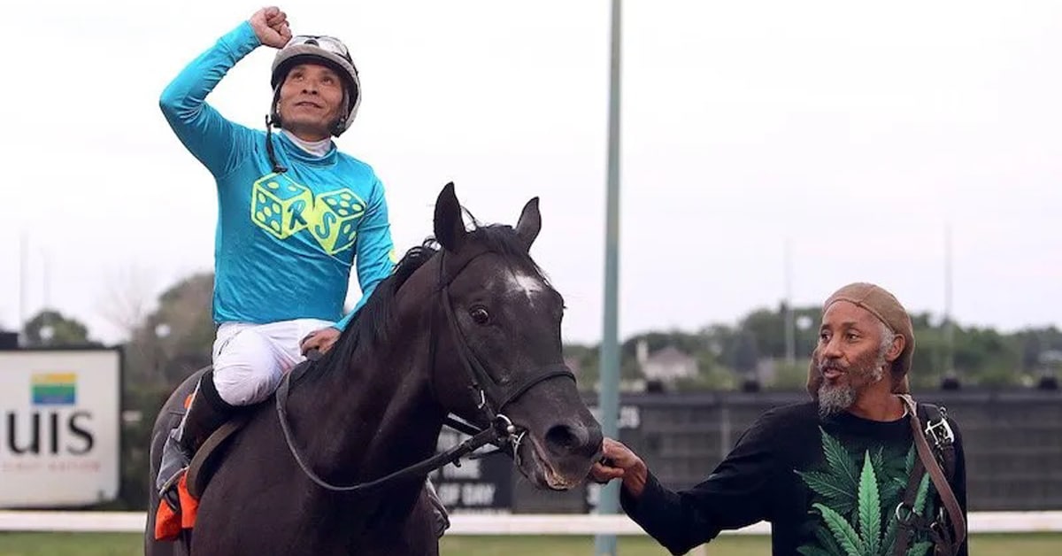 A jockey pointing to the sky on a winning horse.