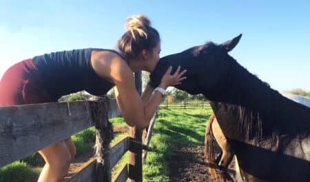 A woman kissing a horse over a fence.