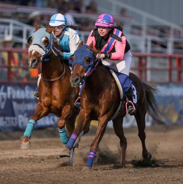 Two young people racing horses on a track.