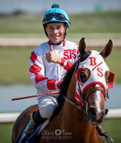 A jockey on a horse giving a thumbs-up.