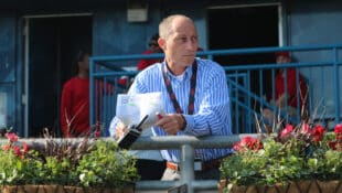 A man at the track holding a racing form and walkie-talkie.