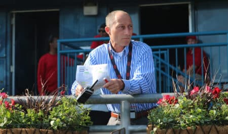 A man at the track holding a racing form and walkie-talkie.