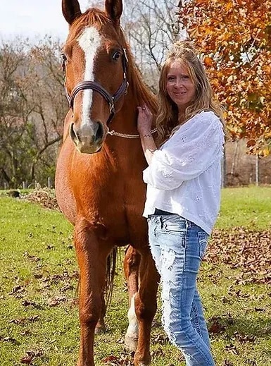 A woman holding a chestnut horse in a field.