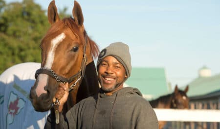 A smiling man holding a racehorse.