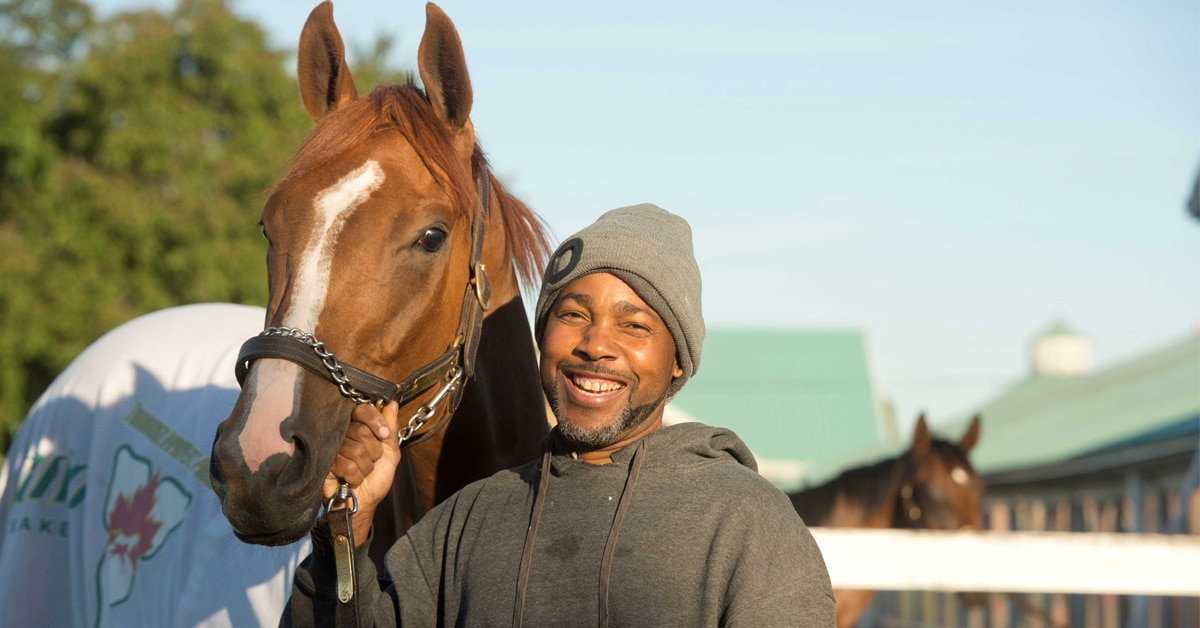 A smiling man holding a racehorse.